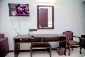 Una habitación con televisión en la pared, un escritorio con silla y un cubo de basura.