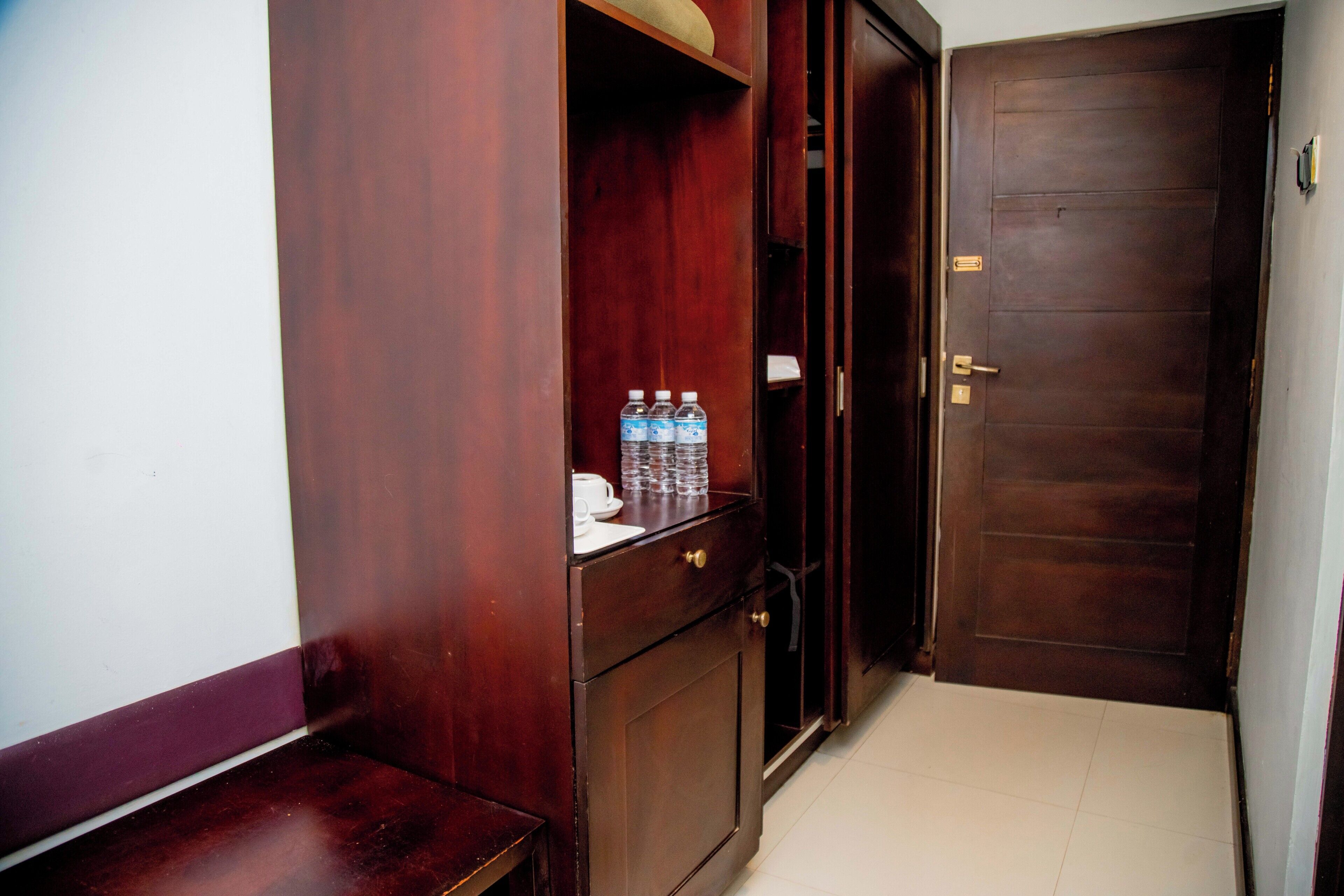 A wooden door with a handle and a keyhole, a small shelf with water bottles, and a white tiled floor.