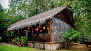 A rustic wooden structure with a thatched roof, surrounded by lush greenery.