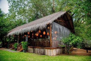 A rustic wooden structure with a thatched roof, surrounded by lush greenery.
