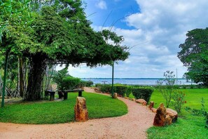 Een pad dat leidt naar een prieel met een bankje, omringd door groen en uitzicht op het water.