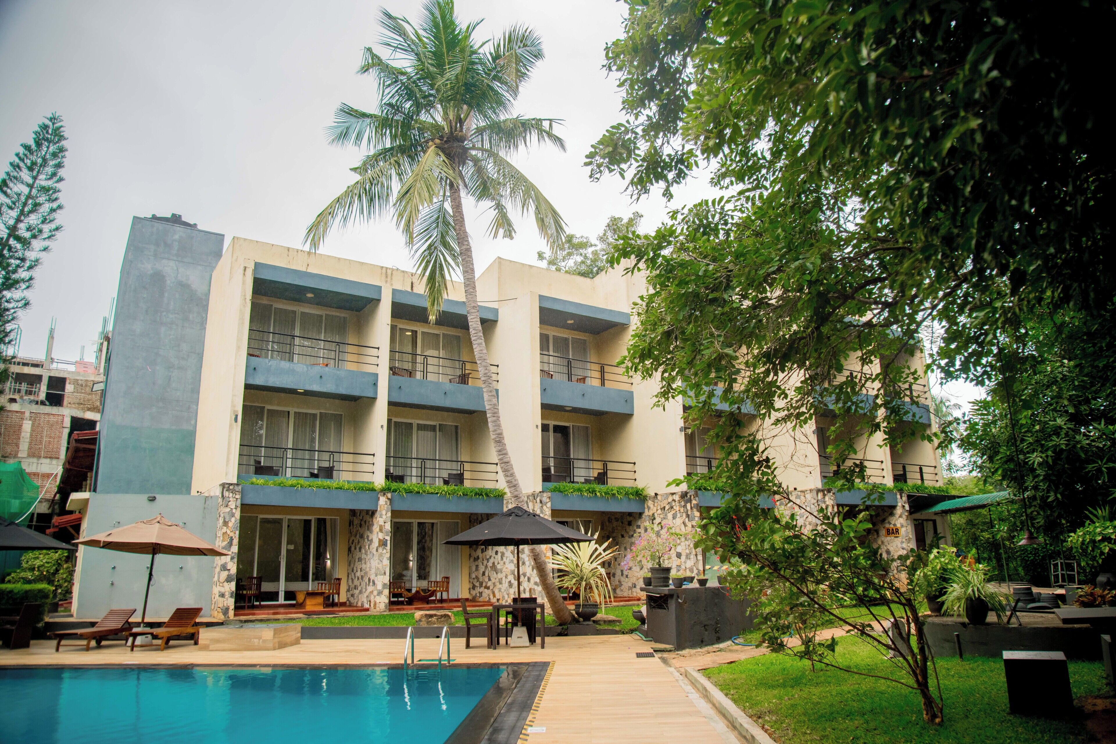 A hotel with a swimming pool, outdoor seating, and a palm tree.