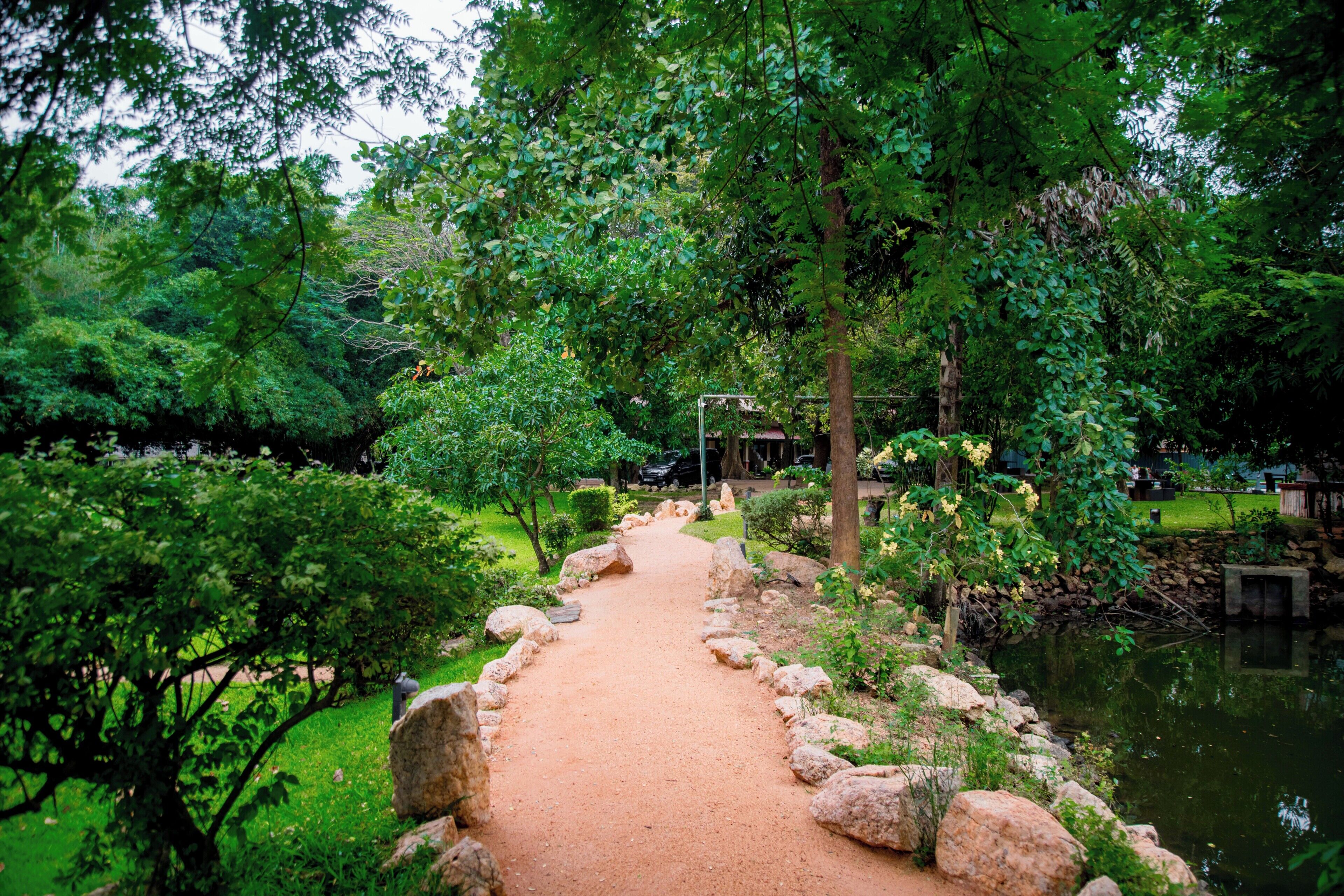Uma trilha serpenteia por um jardim exuberante, com um lago de um lado.