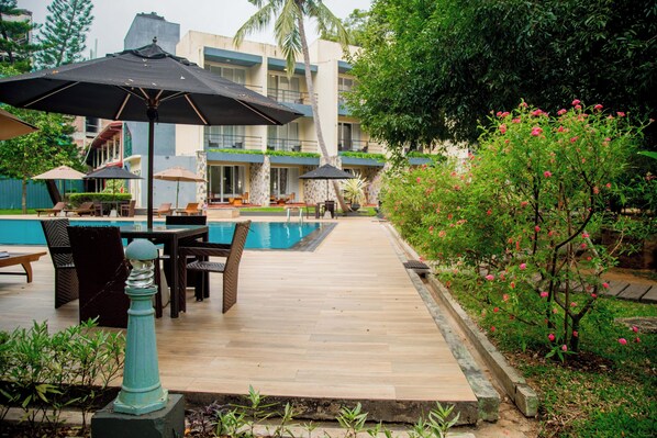 A poolside area with lounge chairs and umbrellas, a wooden deck, and a building in the background.