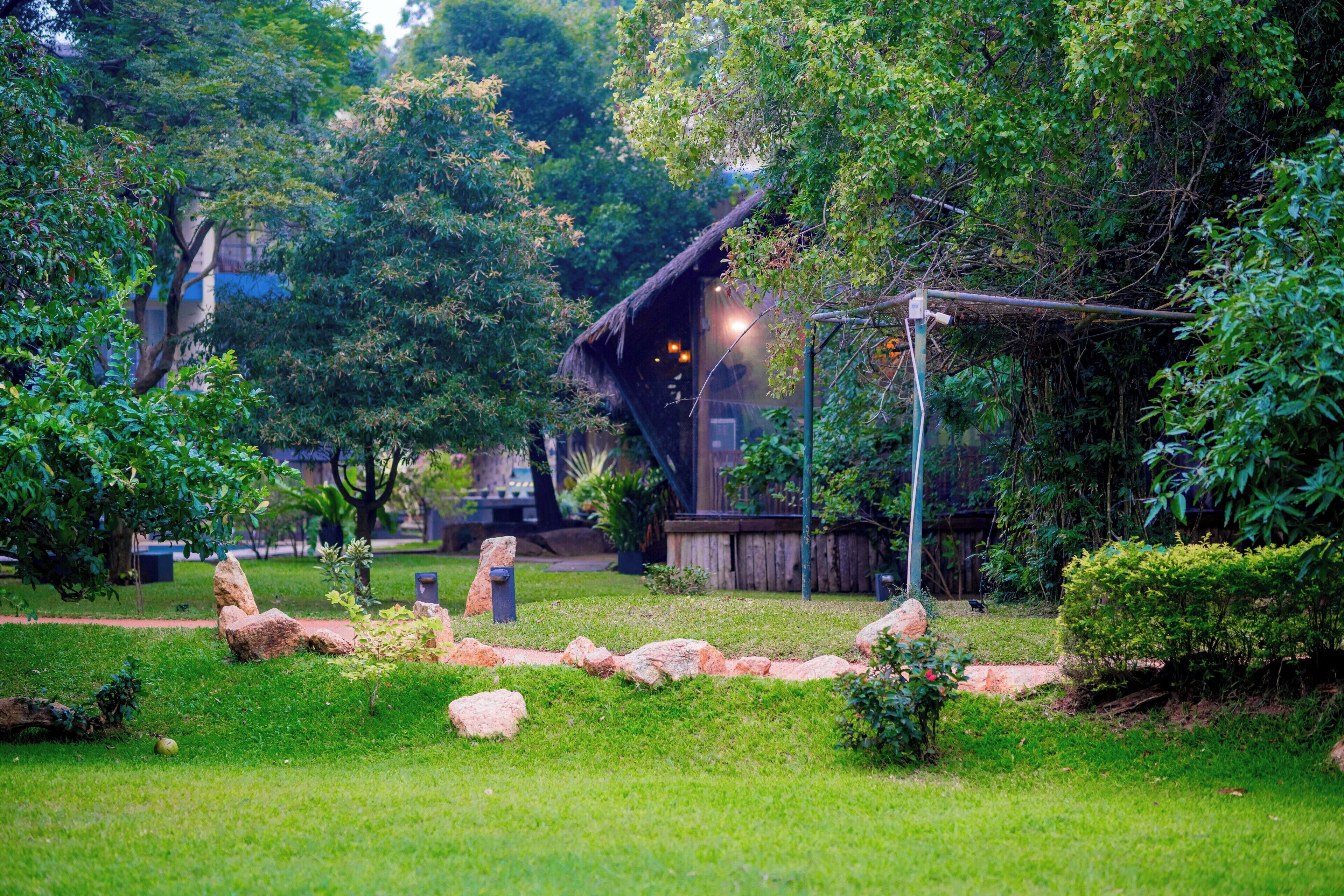 A garden with a pathway, rocks, and a building with a thatched roof.