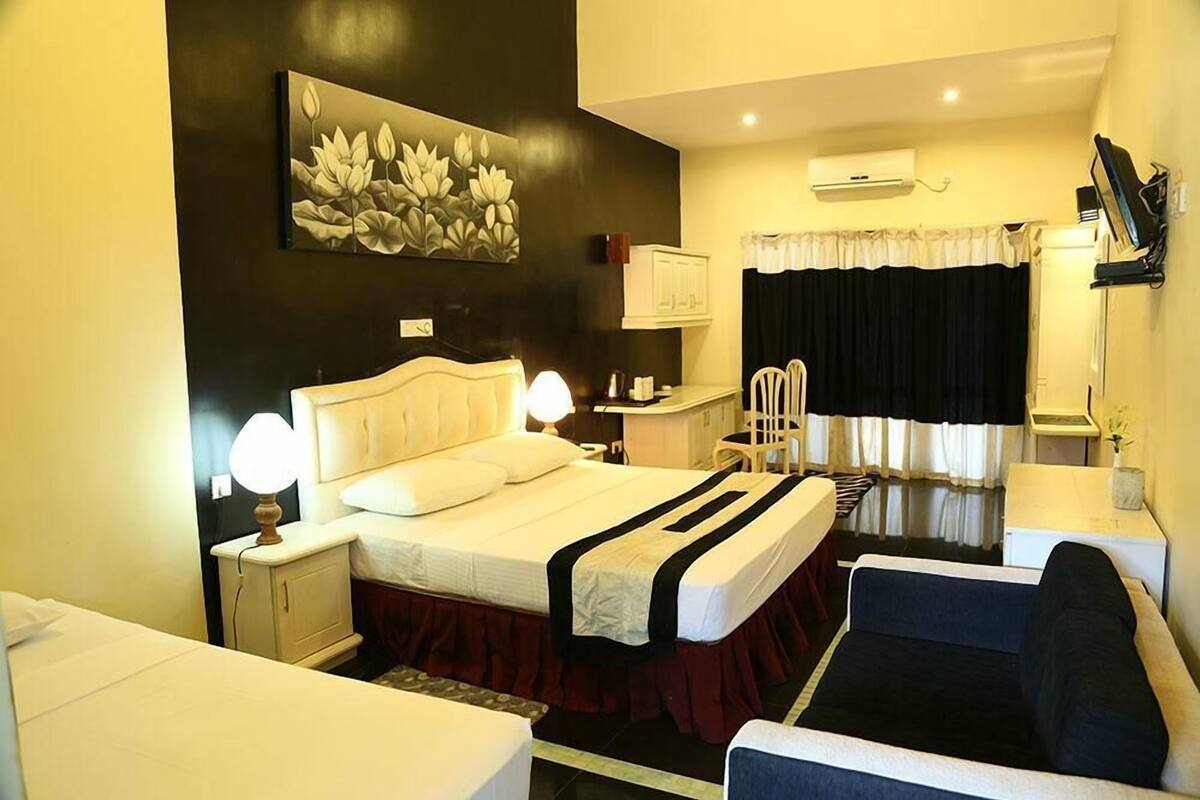 A hotel room with a bed, bedside tables, a chair, a sofa, a painting on the wall, and a window with curtains.