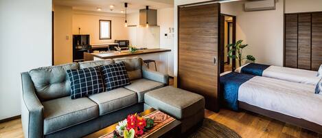 Una sala de estar moderna con un sofá, una mesa de centro con flores, una cama y una cocina al fondo.