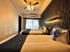 Quarto de hotel com duas camas, um ventilador de teto, um aparelho de ar condicionado e uma parede estampada.