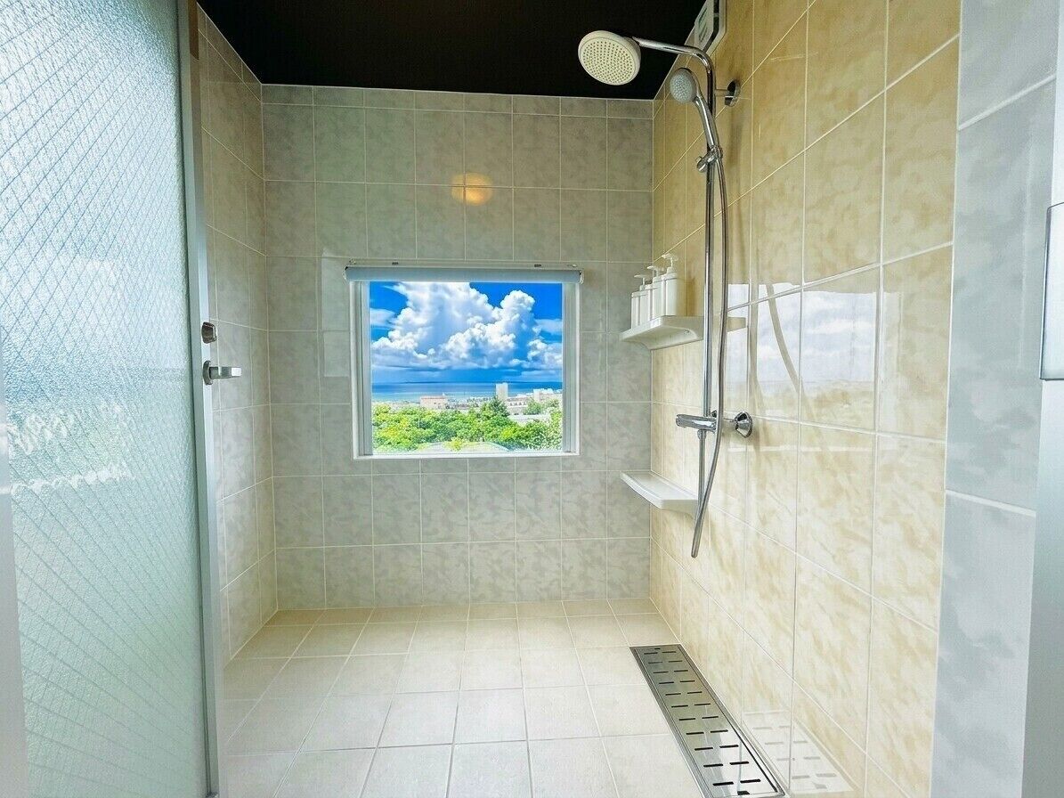 A shower with a window, tiled walls, and a view of greenery.