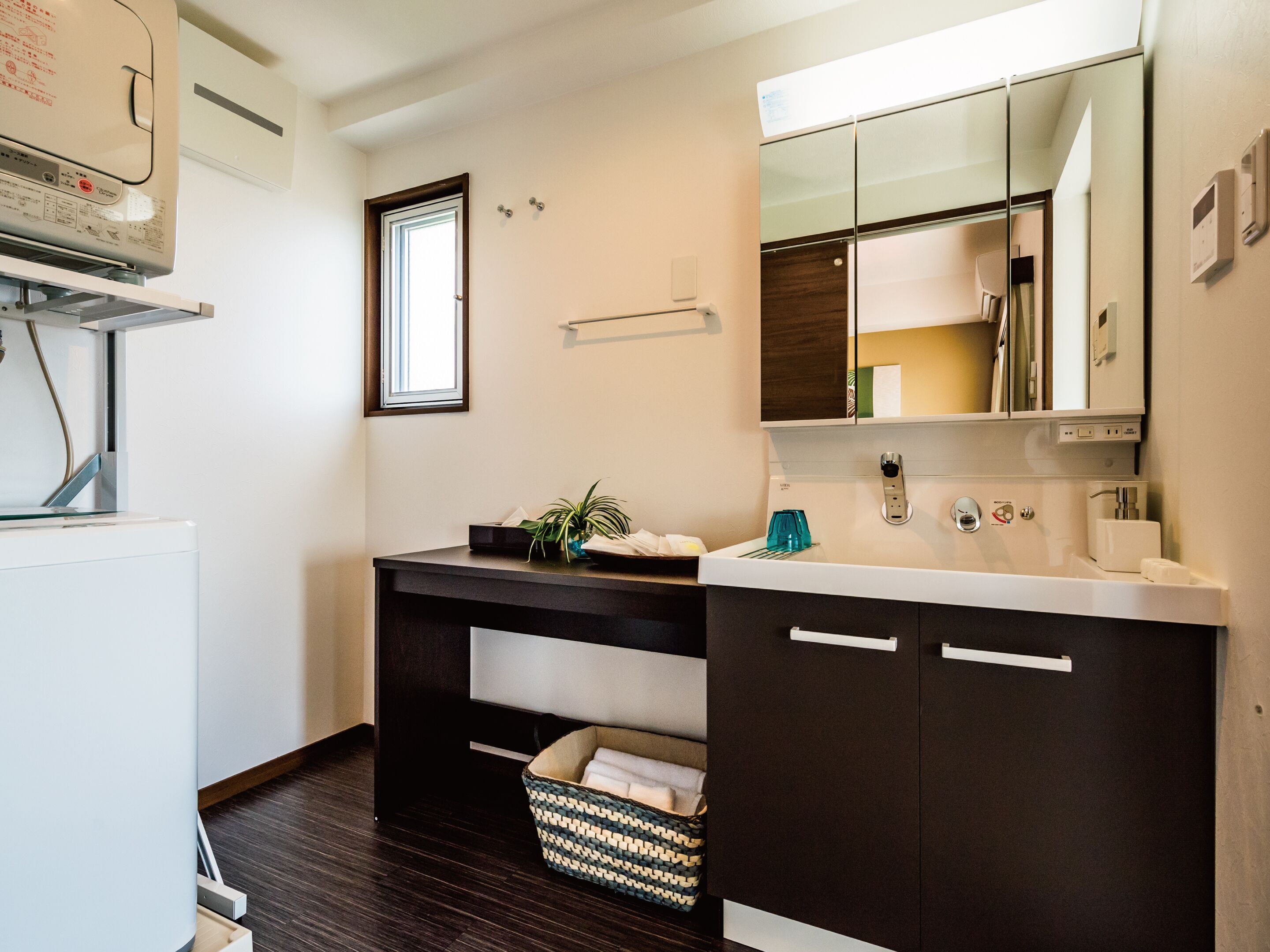 A modern bathroom with a white sink, dark cabinets, a mirror, and a small window.
