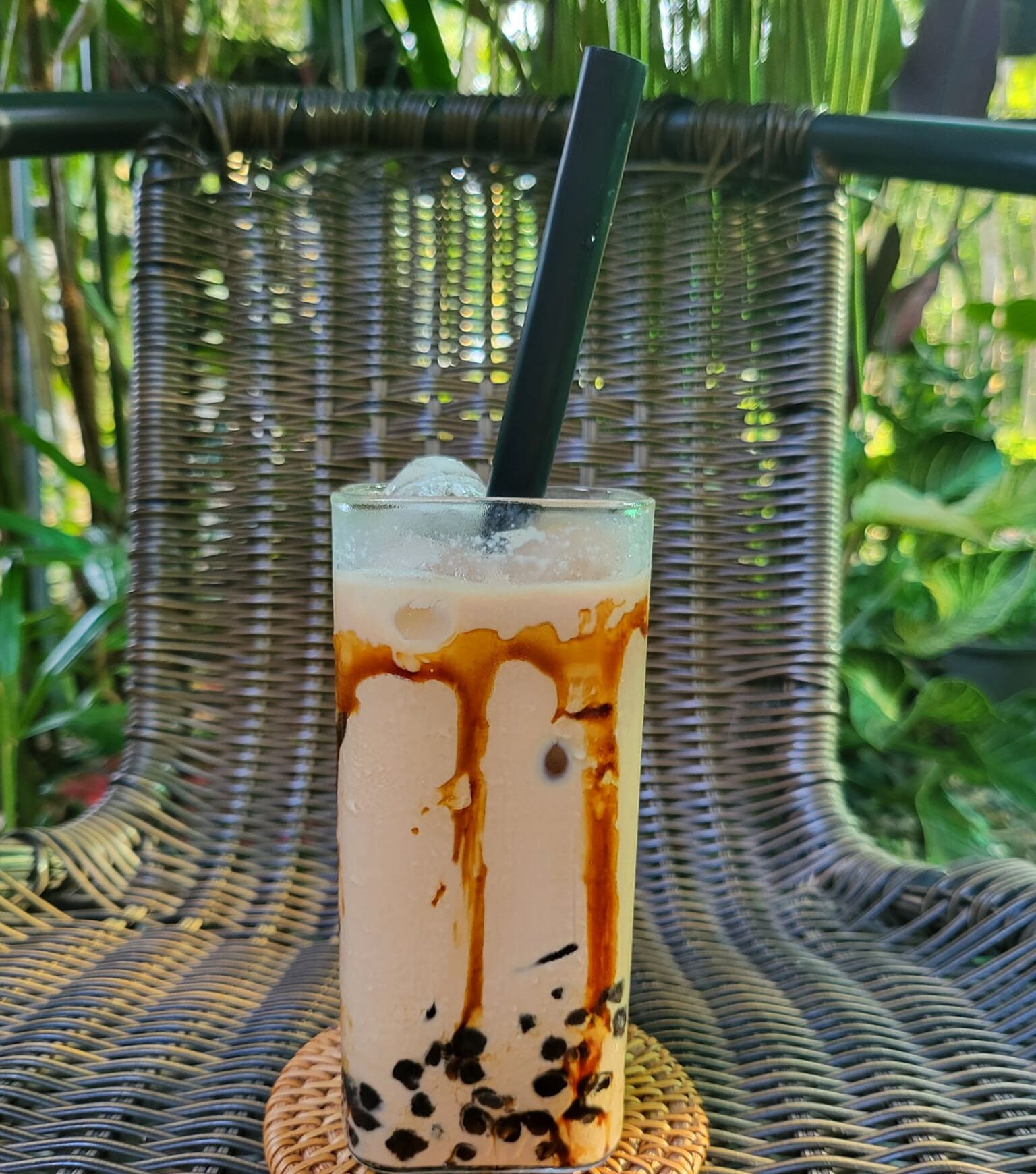 Un vaso de café helado con leche y almíbar de chocolate, sobre una silla tejida al aire libre.