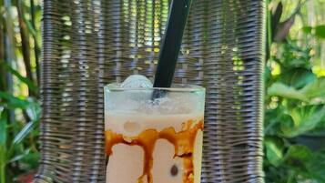 Un vaso de café helado con leche y almíbar de chocolate, sobre una silla tejida al aire libre.