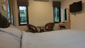 A hotel room with a bed, two wicker chairs, a small table, an air conditioning unit, a TV, and windows with curtains.