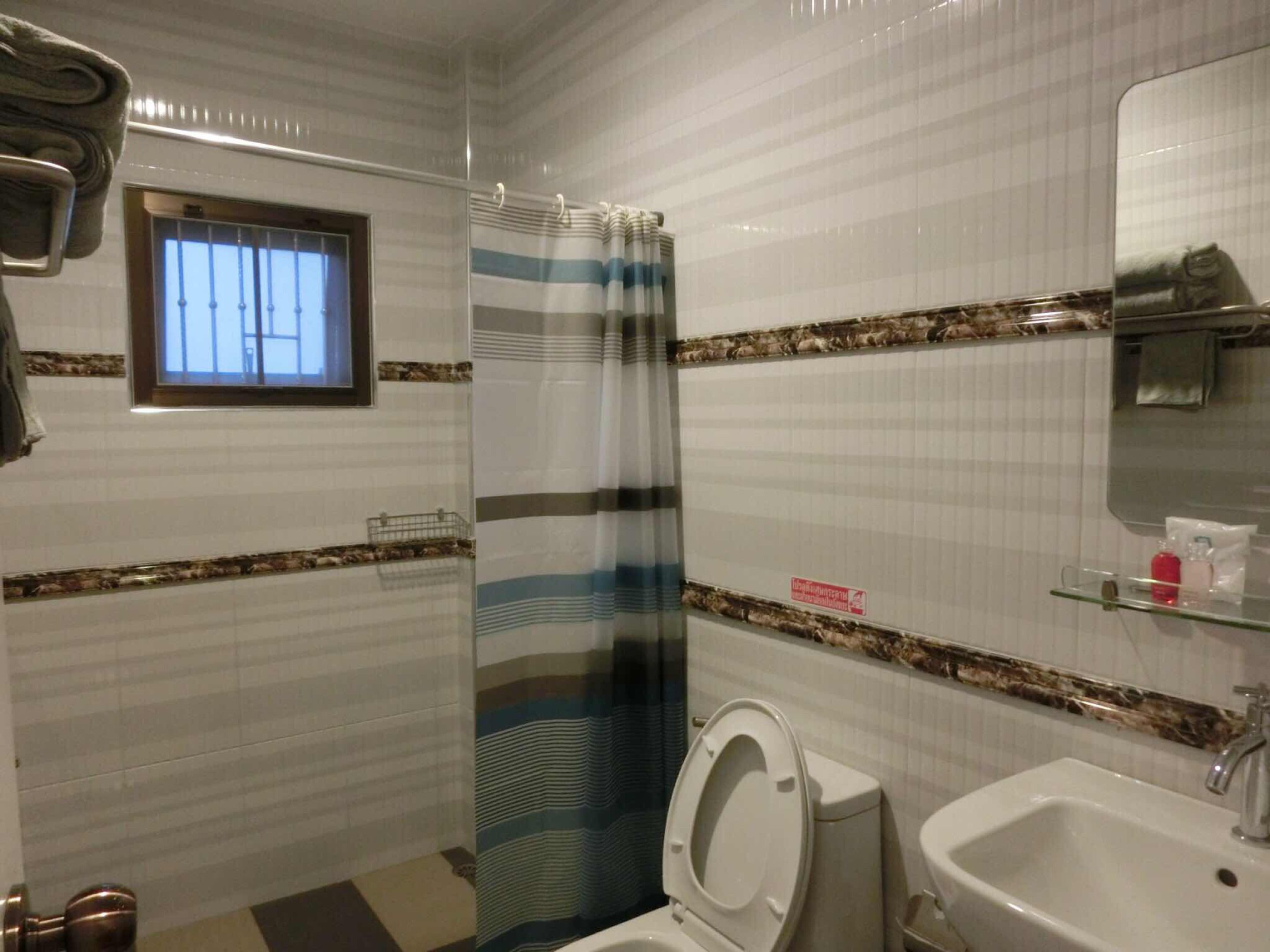 A bathroom with a striped shower curtain, a toilet, a sink, and a window with bars.