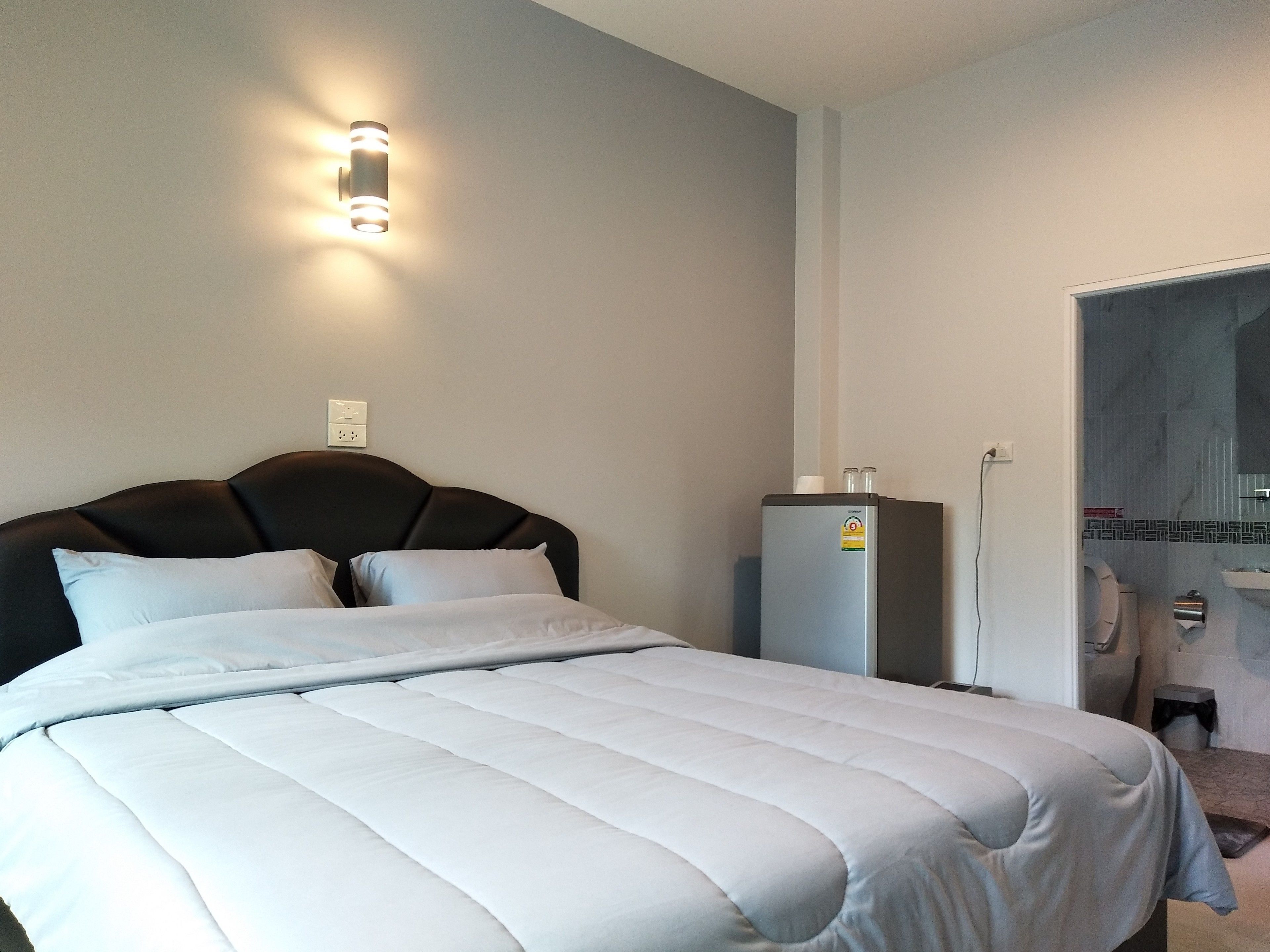 A bedroom with a bed, a wall-mounted light, a water dispenser, and a bathroom visible through an open door.