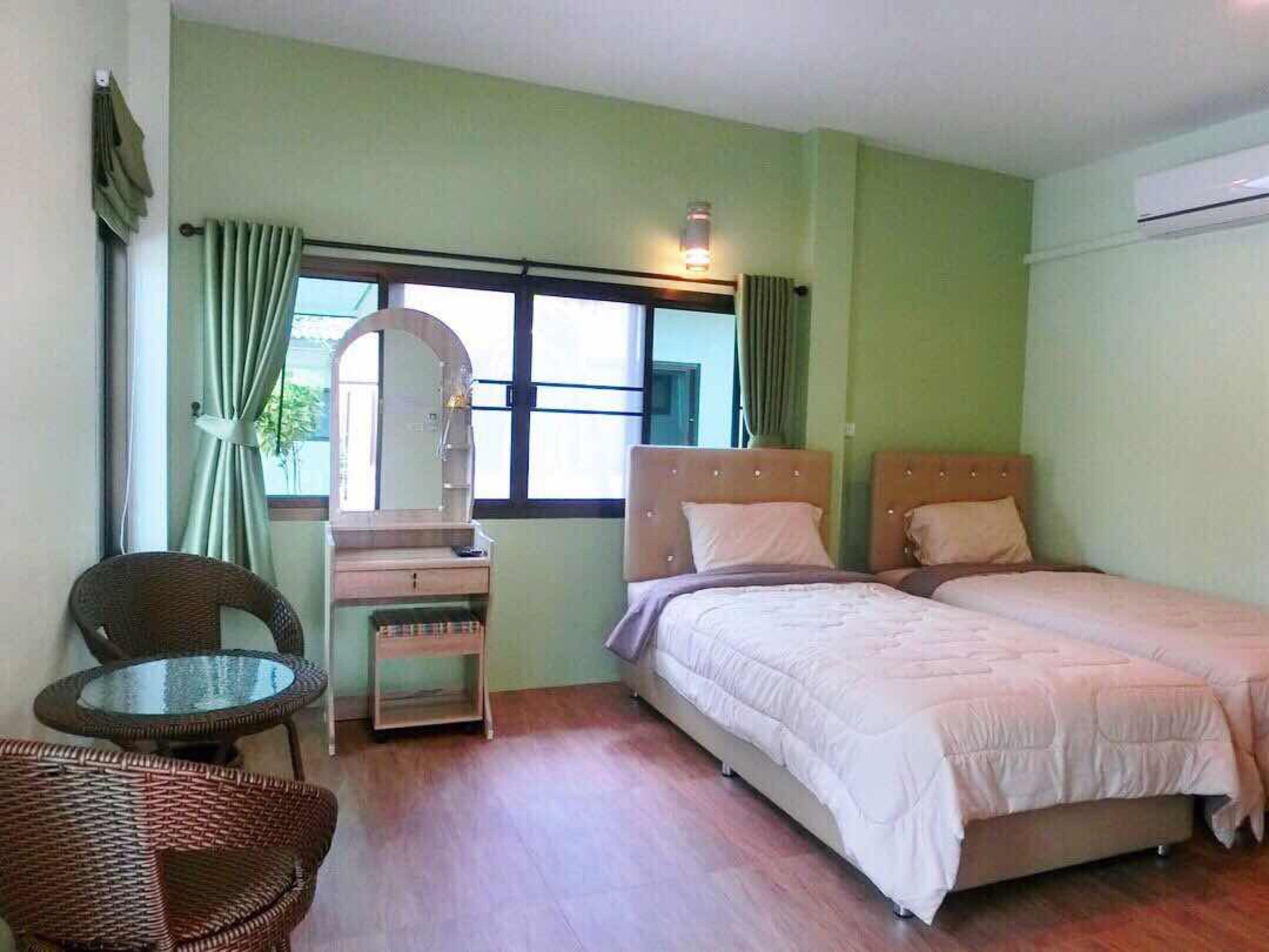 A bedroom with two beds, a small table, a chair, a mirror, and a window with curtains.