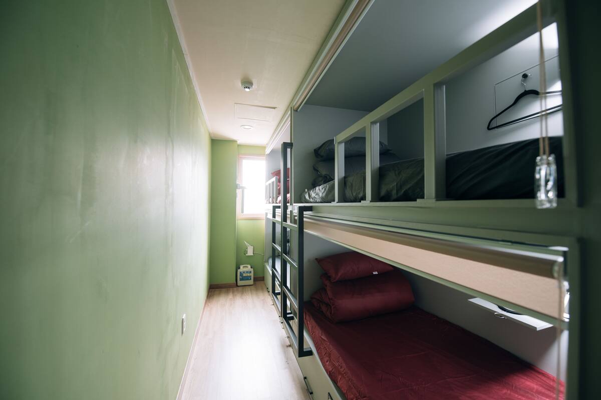 A narrow corridor with bunk beds on one side and a window at the end.