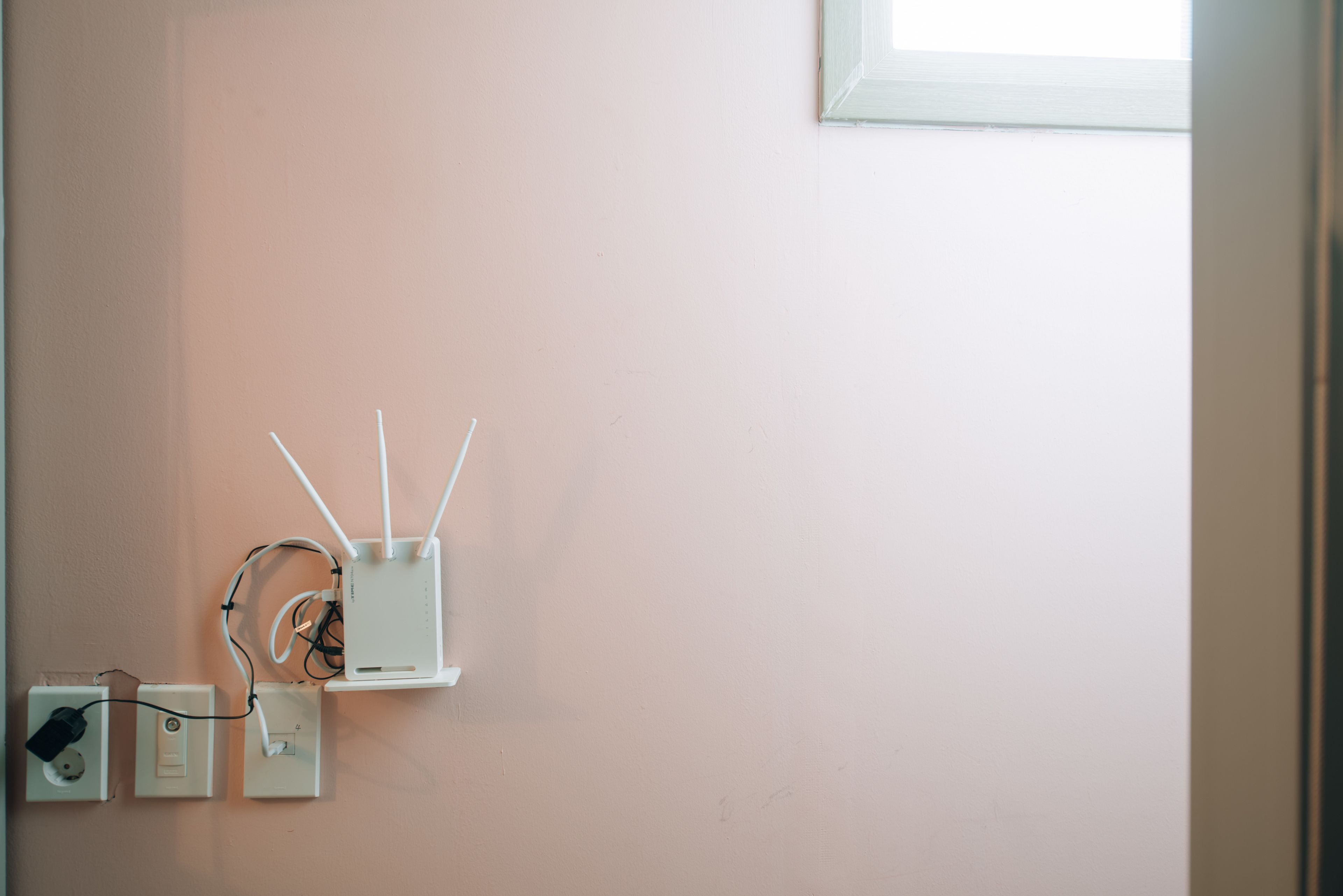 Un enrutador y tomas de corriente instalados en una pared rosa claro.