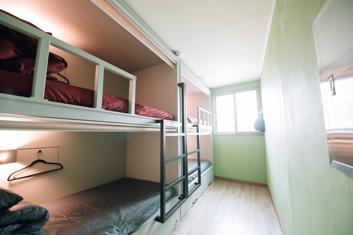 A bunk bed room with a wooden floor, a white wall, and a window.