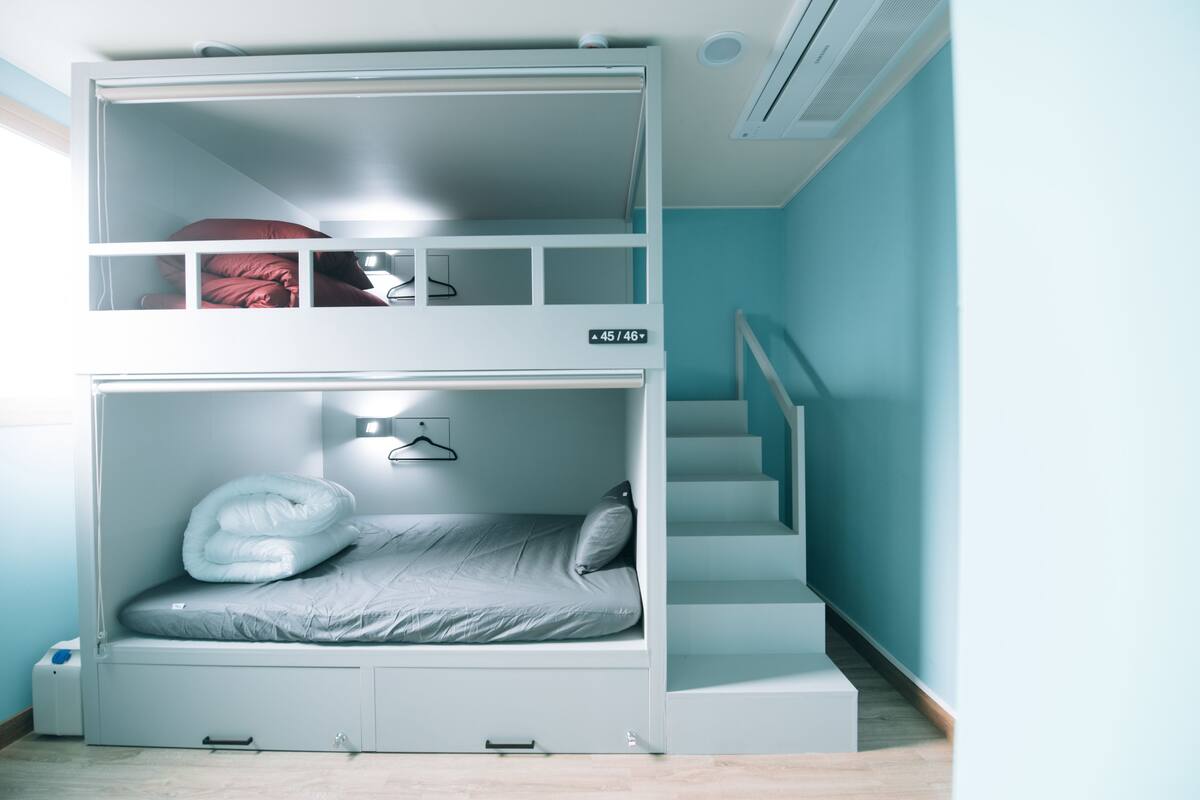A bunk bed room with a built-in desk and shelving, a staircase, and a wall-mounted heater.