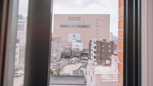A view of a Hyundai department store building with a large billboard, surrounded by other buildings and parked cars. - Midtown Hostel (Daegu)