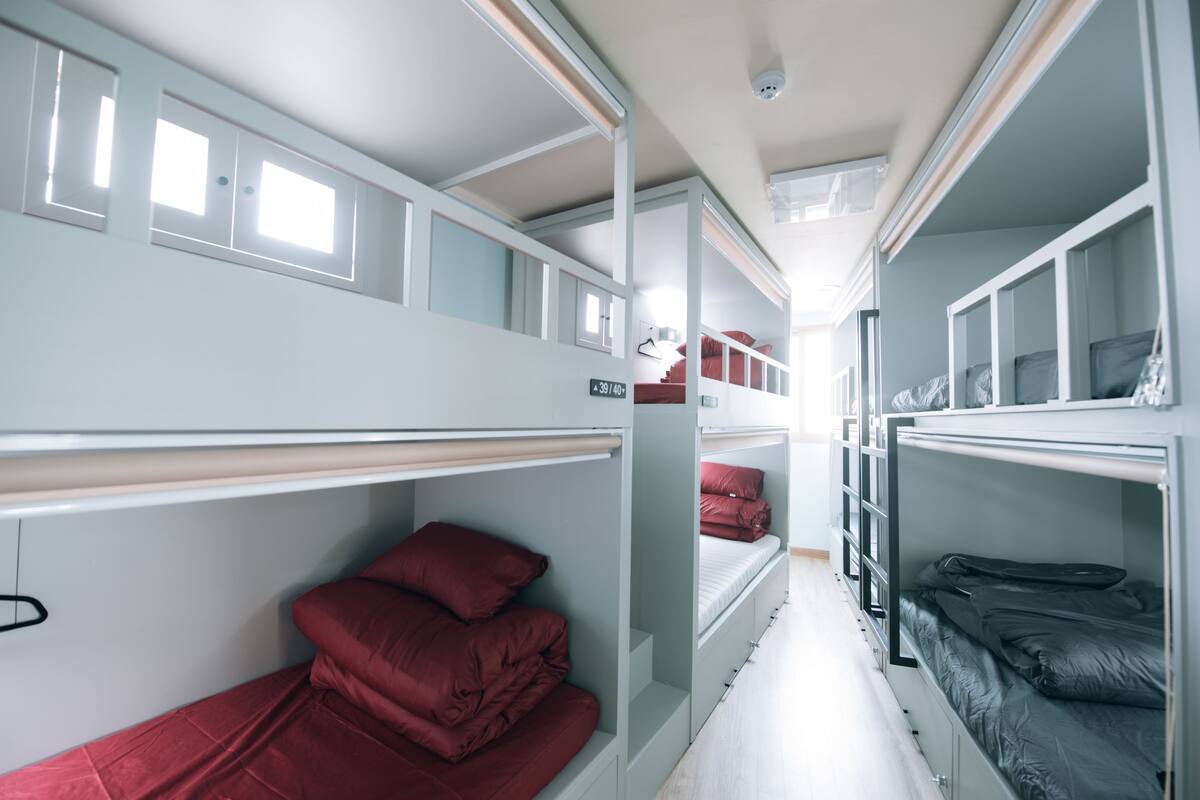 A narrow, multi-level bunk room with bunk beds, a small desk, and a window.