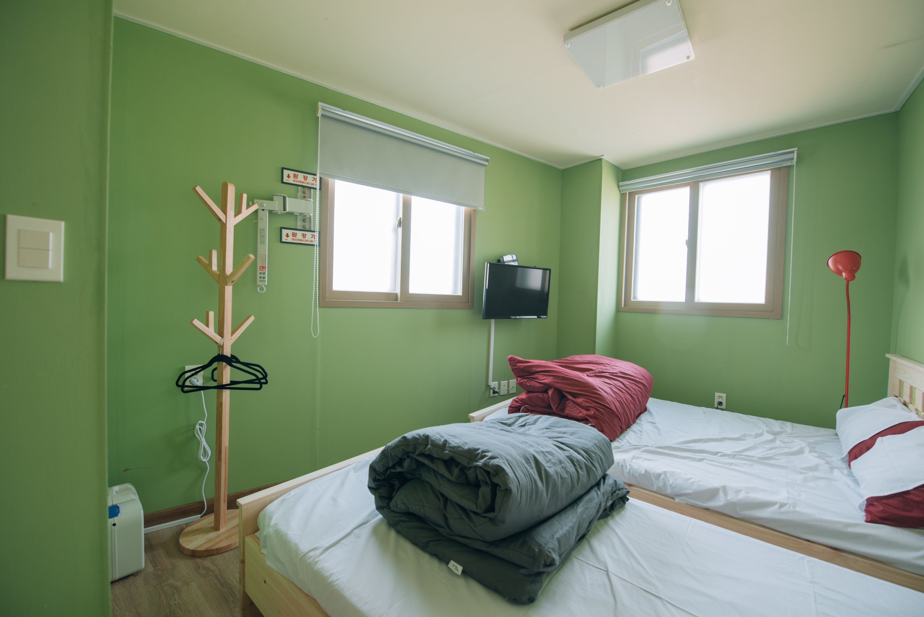 A room with two beds, a TV, a coat rack, and a window with blinds.