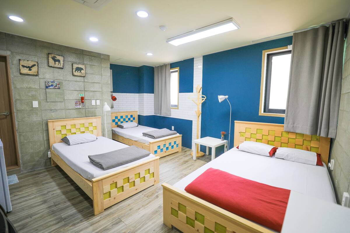 A hotel room with three wooden beds, a small table, a window with curtains, and a wall with animal pictures.