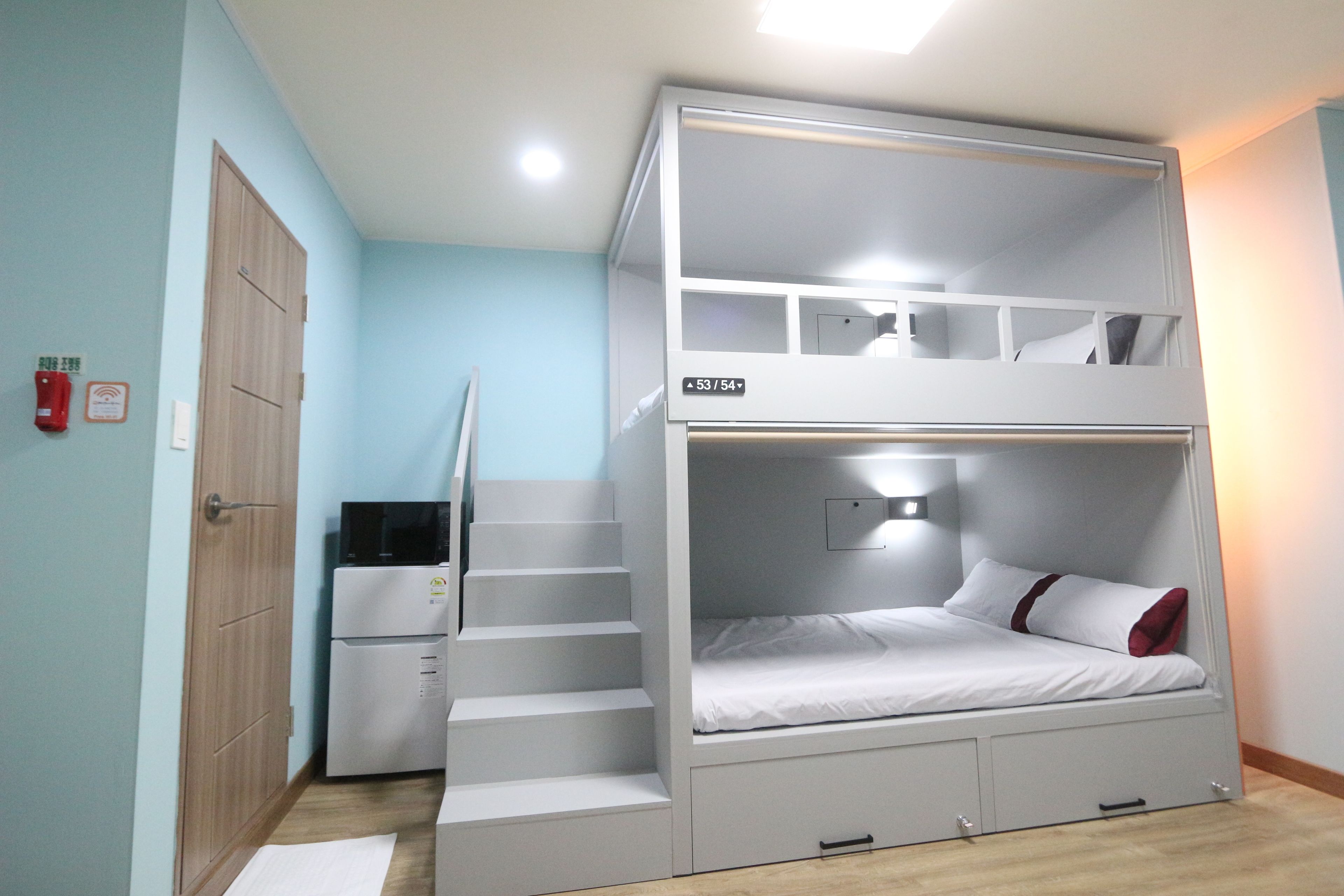 A bunk bed with a desk and a chair, a wooden wardrobe, and a small refrigerator.