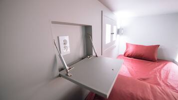 A compact room with a bed, a small desk, and a wall-mounted light fixture.