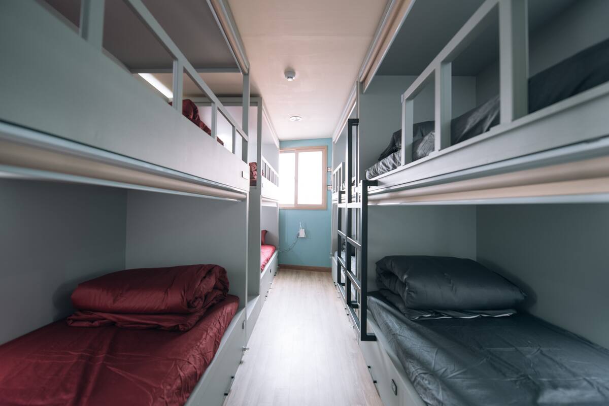 A narrow room with bunk beds, a small window, and a light switch on the wall.