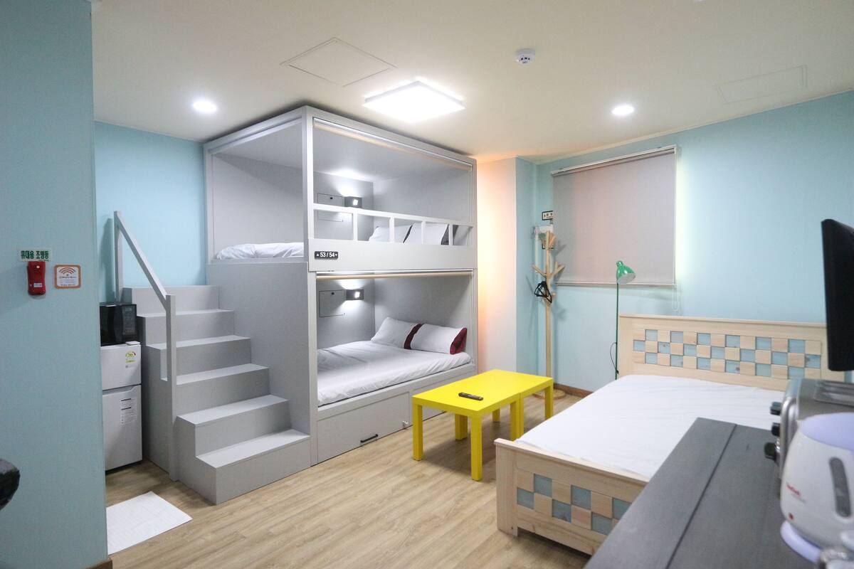 A room with a bunk bed, a desk, a chair, a small table, and a bed.