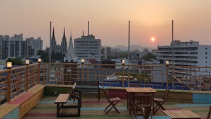 A rooftop terrace with wooden furniture and a cityscape view at sunset. - Midtown Hostel (Daegu)