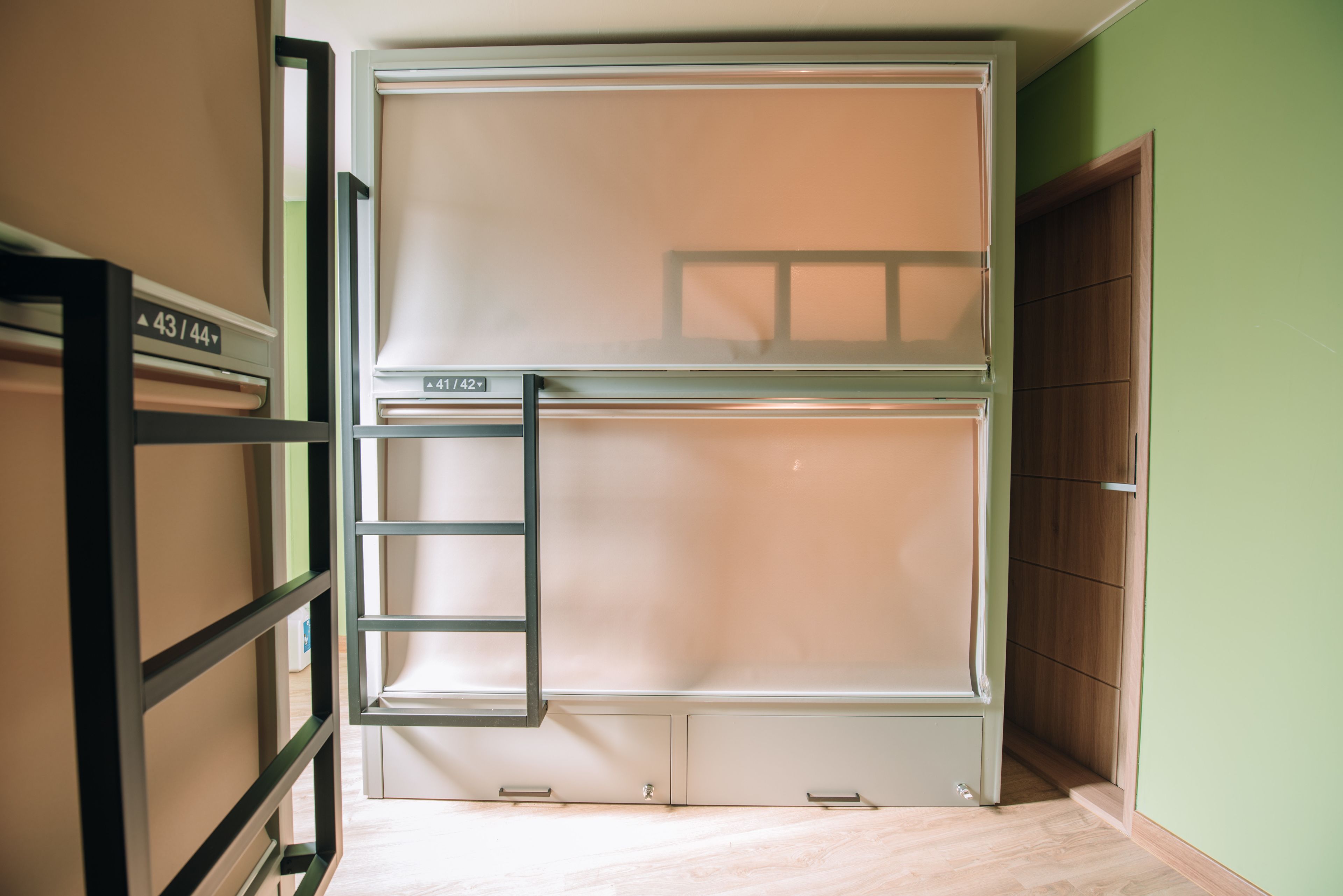 Una cama litera con escalera, un armario de madera y una puerta en una habitación con paredes verdes y suelo de madera.
