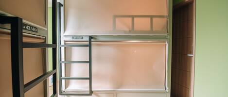 Una cama litera con escalera, un armario de madera y una puerta en una habitación con paredes verdes y suelo de madera.