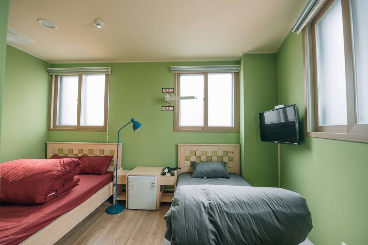A room with two beds, a small desk, a TV, and two windows.