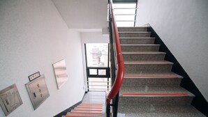 A staircase with red handrails and a view of the outside through a glass door at the top. - Midtown Hostel (Daegu)