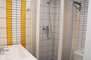 Un baño con ducha, lavamanos y paredes con azulejos blancos y amarillos.