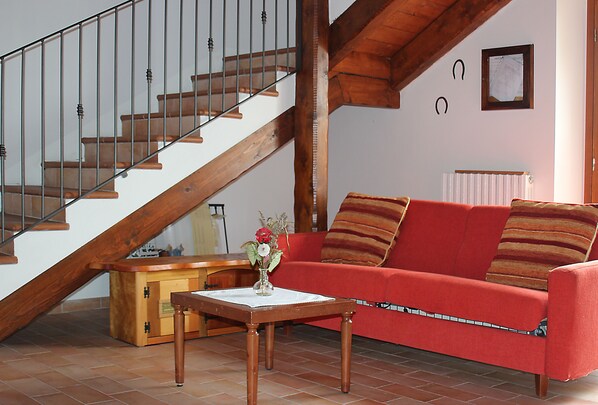 A staircase with wooden steps and metal railings, a red sofa with striped cushions, and a small wooden table with a vase of flowers. - Agriturismo Prato Grande (Loiano)