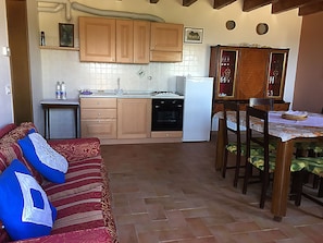A compact kitchen with wooden cabinets, a white refrigerator, and a dining table with chairs. - Agriturismo Prato Grande (Loiano)