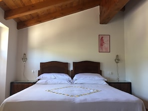 A double bed with a white bedspread and a decorative border, two bedside tables with lamps, wooden beams on the ceiling, and a framed picture on the wall. - Agriturismo Prato Grande (Loiano)