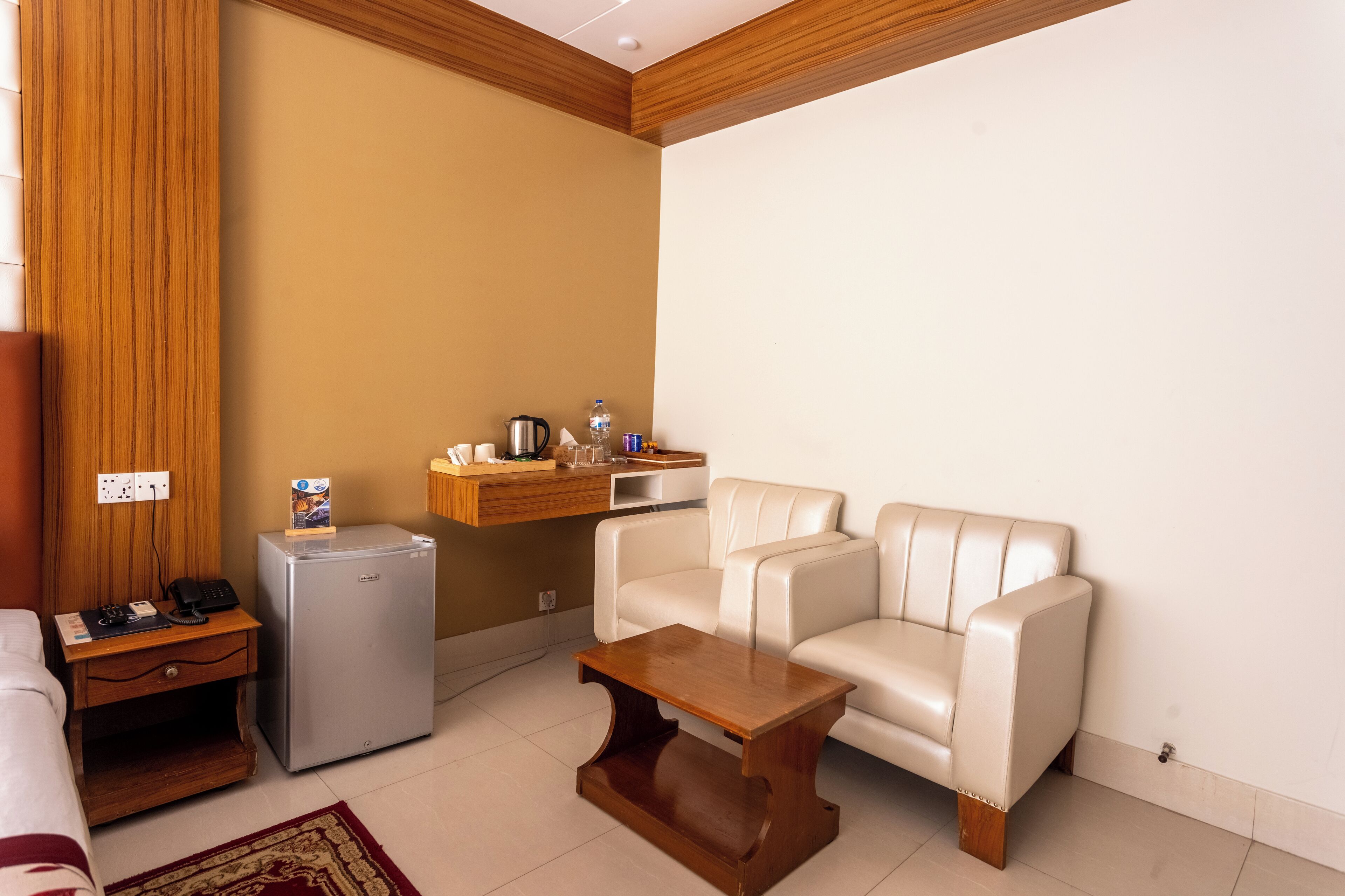 Un espacio habitable compacto con sofá, refrigerador pequeño, mesita de noche de madera y una mesa de centro.