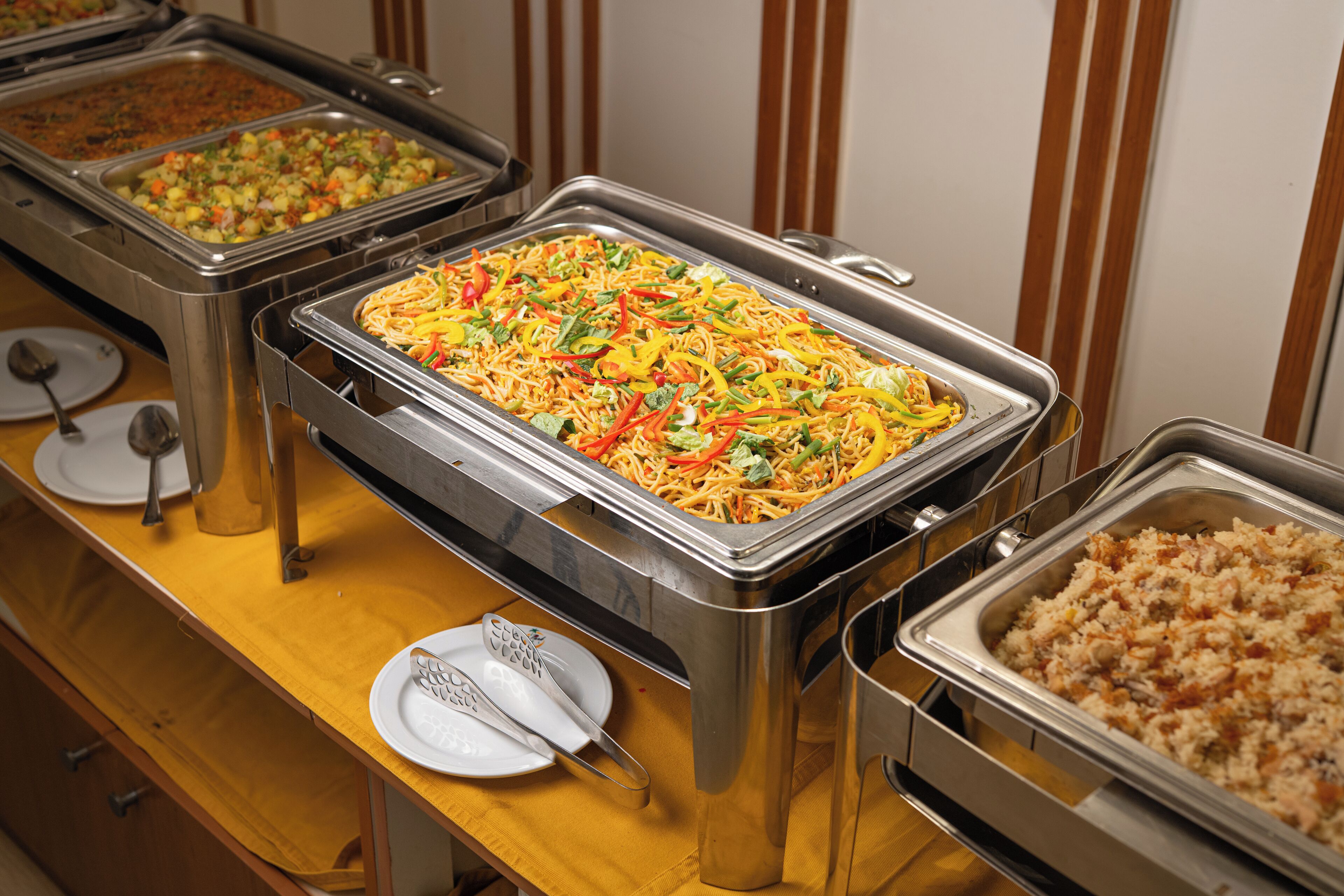 A buffet with various dishes including noodles, rice, and mixed vegetables.