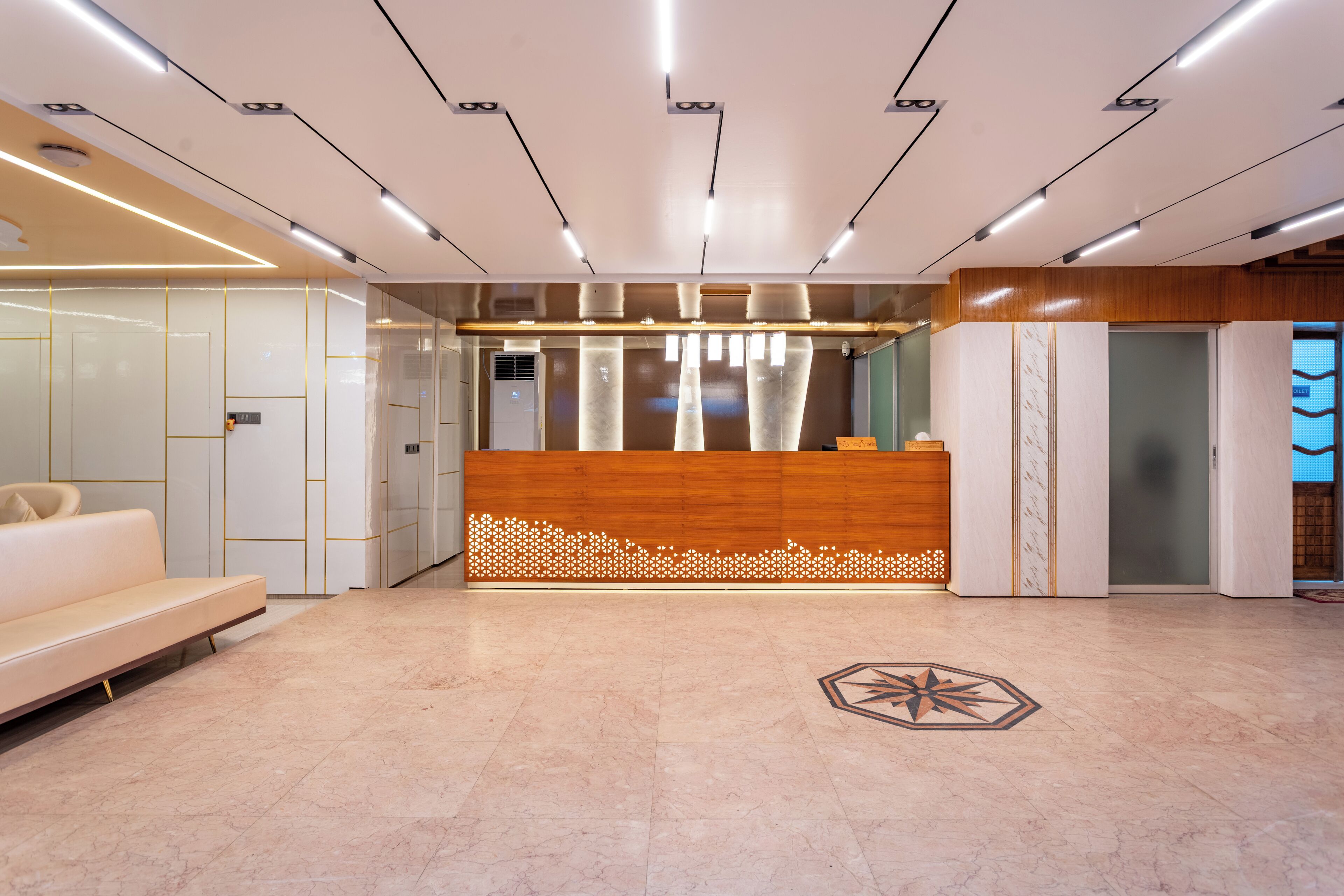 Un área de recepción moderna con un mostrador de madera, un sofá blanco y un diseño geométrico en el suelo.