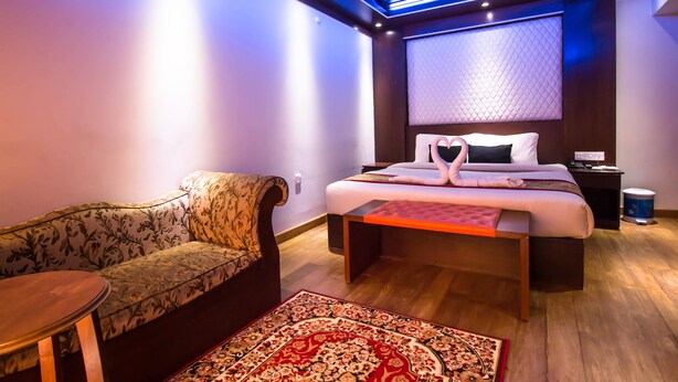Et moderne hotelværelse med en sofa, en seng med en hjerteformet pude-opstilling, et lille bord og en tæppe med et mønster.