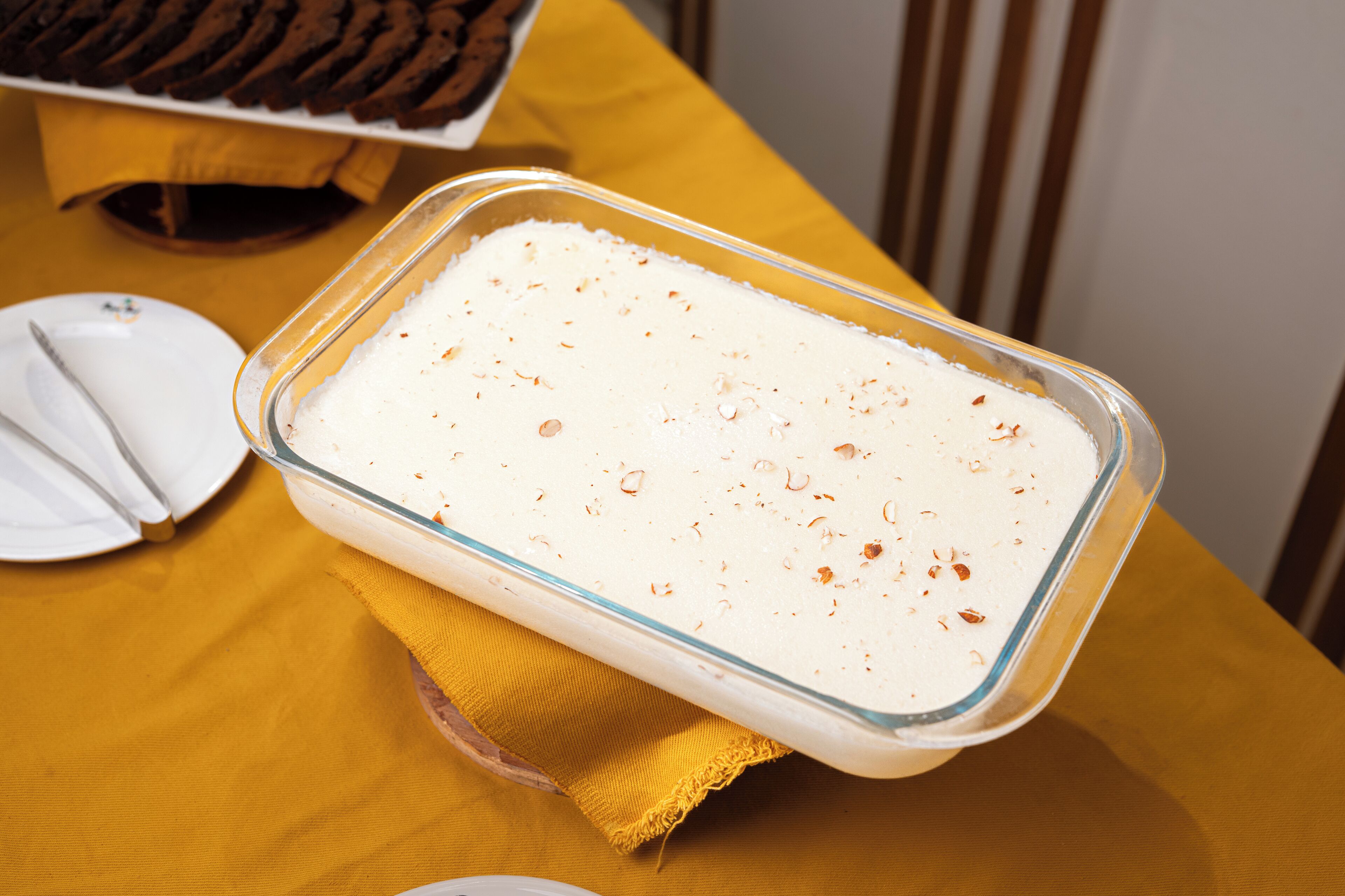 Et glasfad med en hvid dessert på en gul dug.
