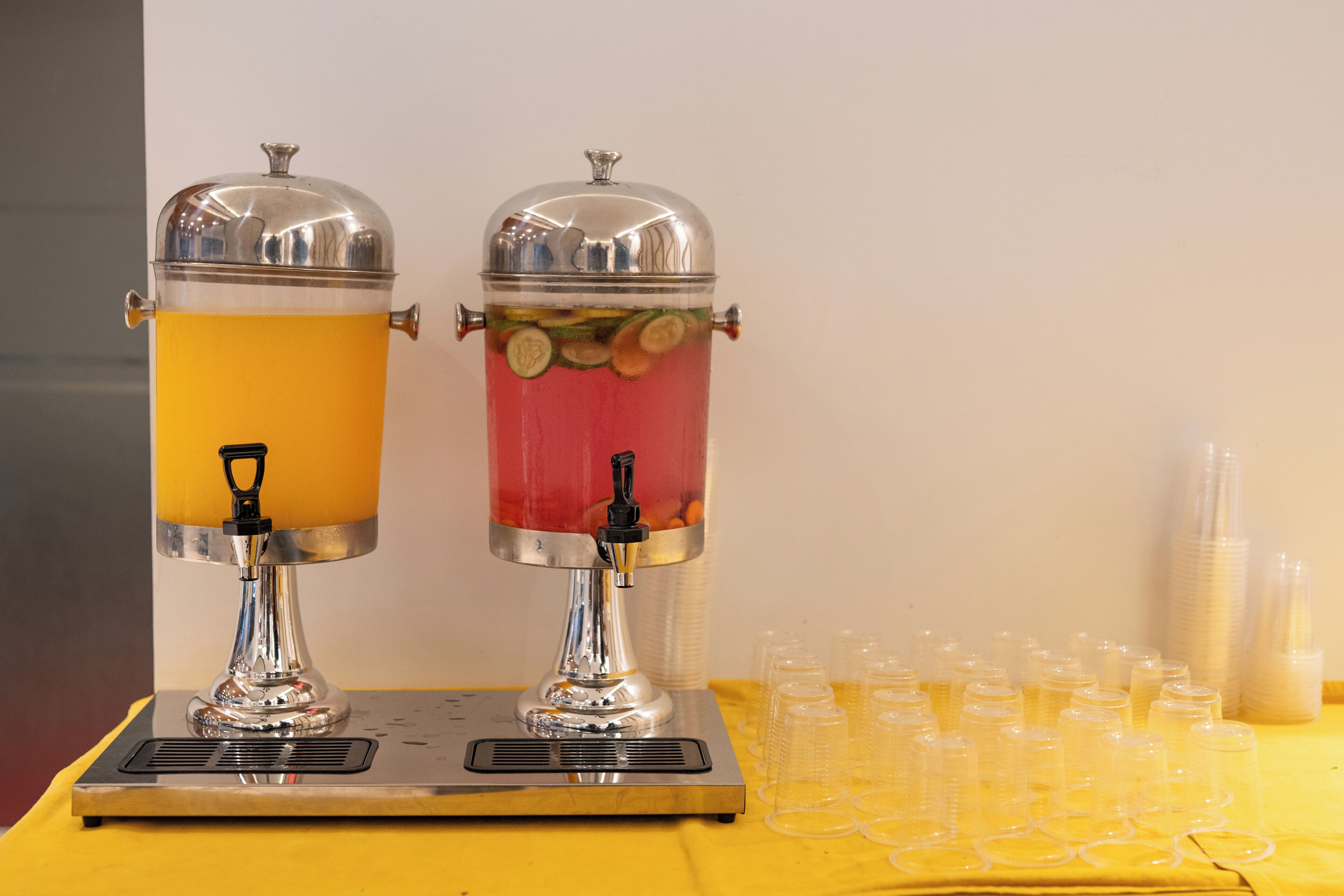 Deux distributeurs de boissons avec robinets et une table avec des gobelets en plastique.