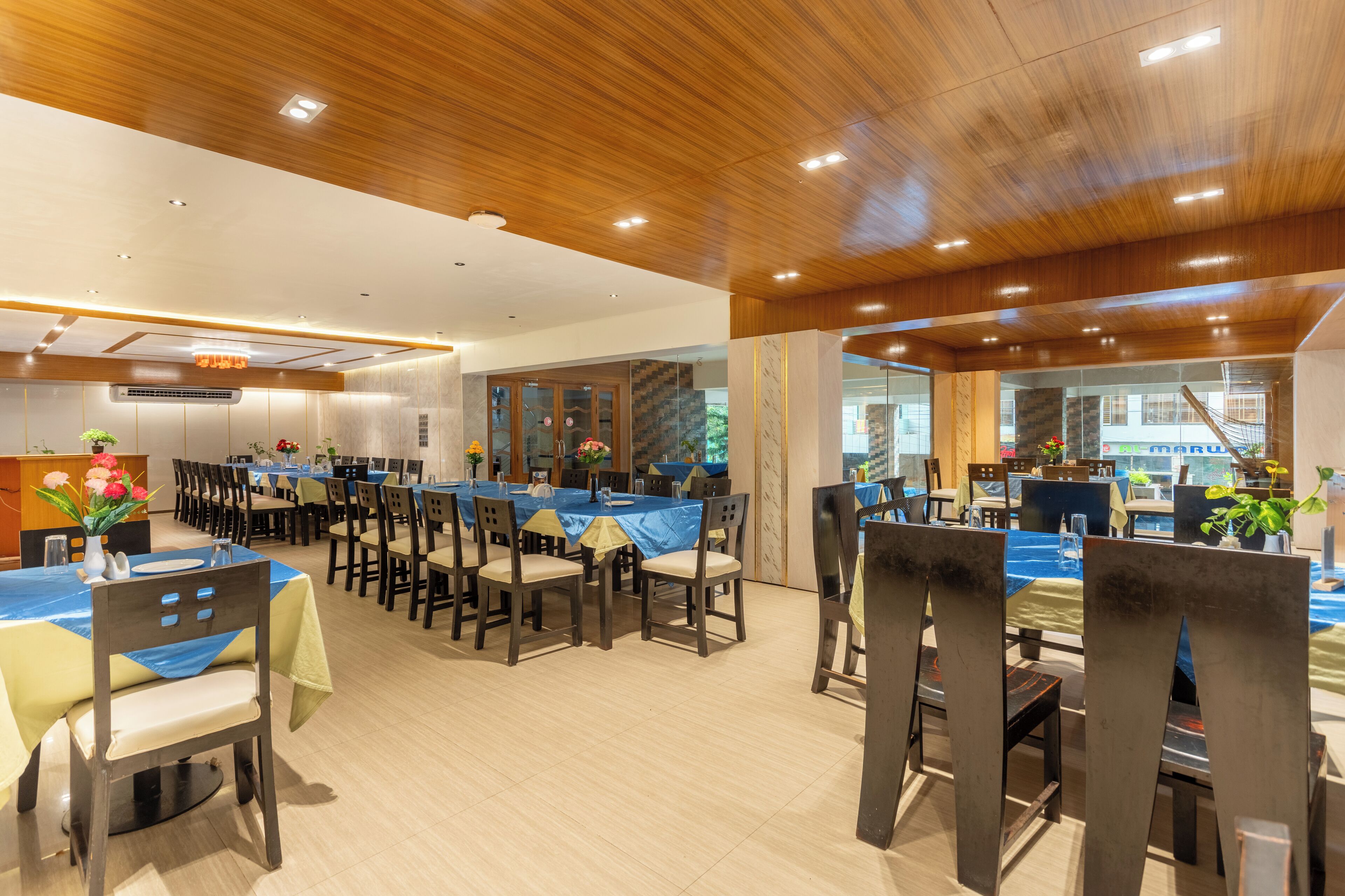 A spacious dining area with multiple tables and chairs, wooden ceiling, and large windows.