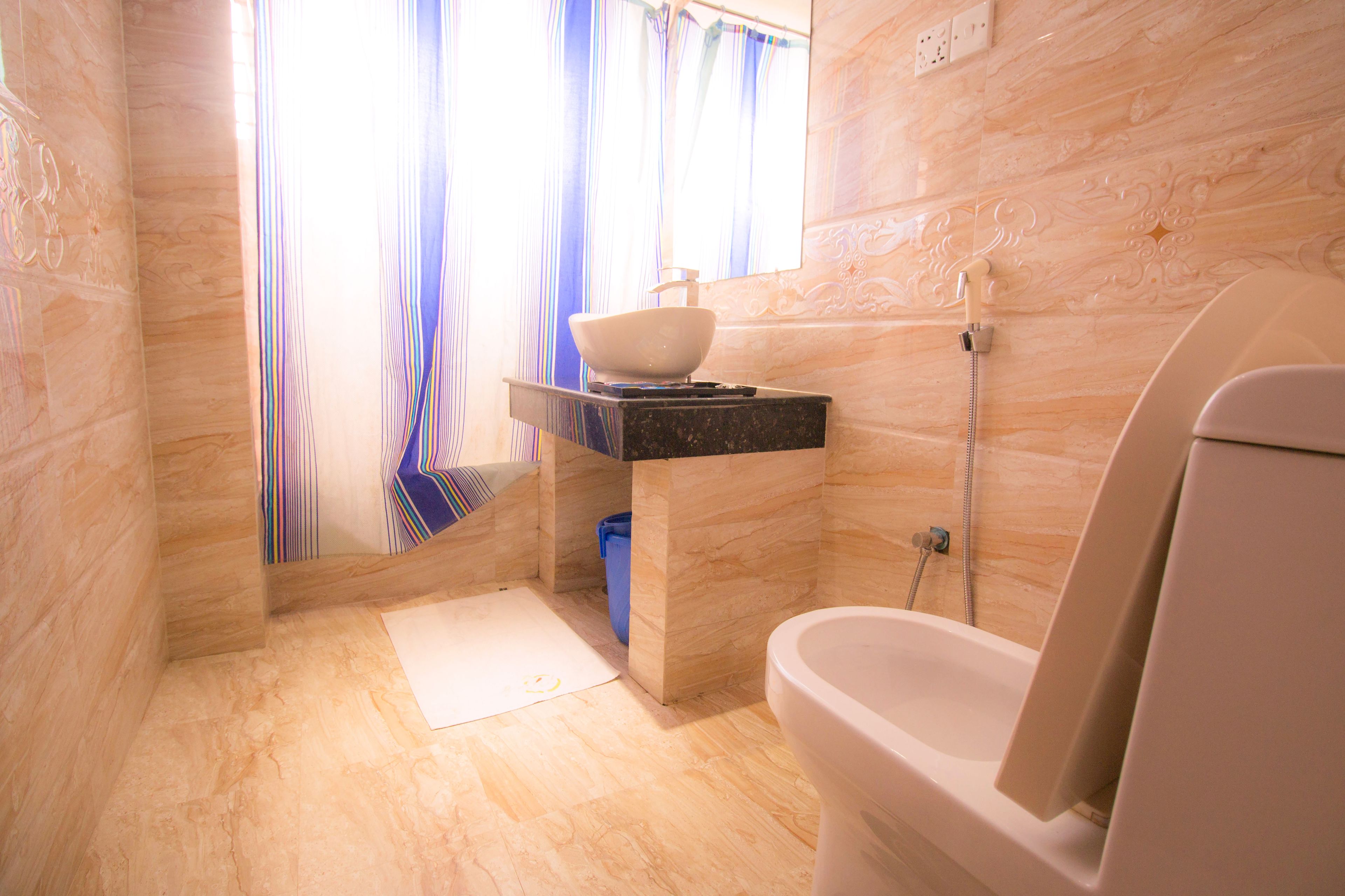 A bathroom with a toilet, a sink with a bowl, a shower, and a window with curtains.