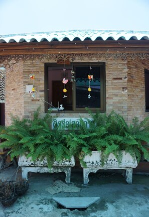 Un edificio con fachada de ladrillo, una ventana adornada con decoraciones colgantes y dos macetas blancas con plantas verdes en primer plano.